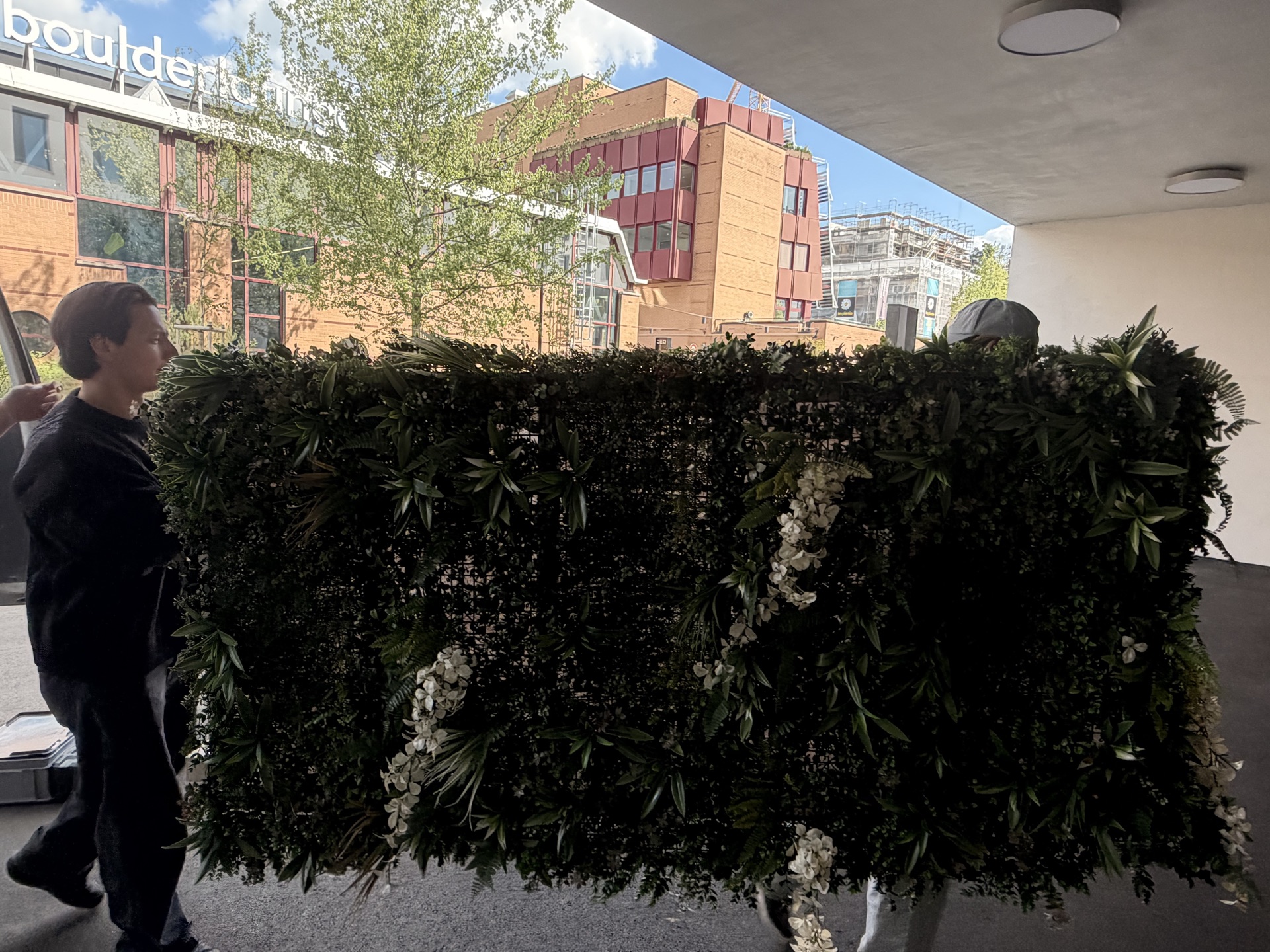 Die grüne Blumenwand wird vor dem Bouldercenter zur Eventhalle getragen