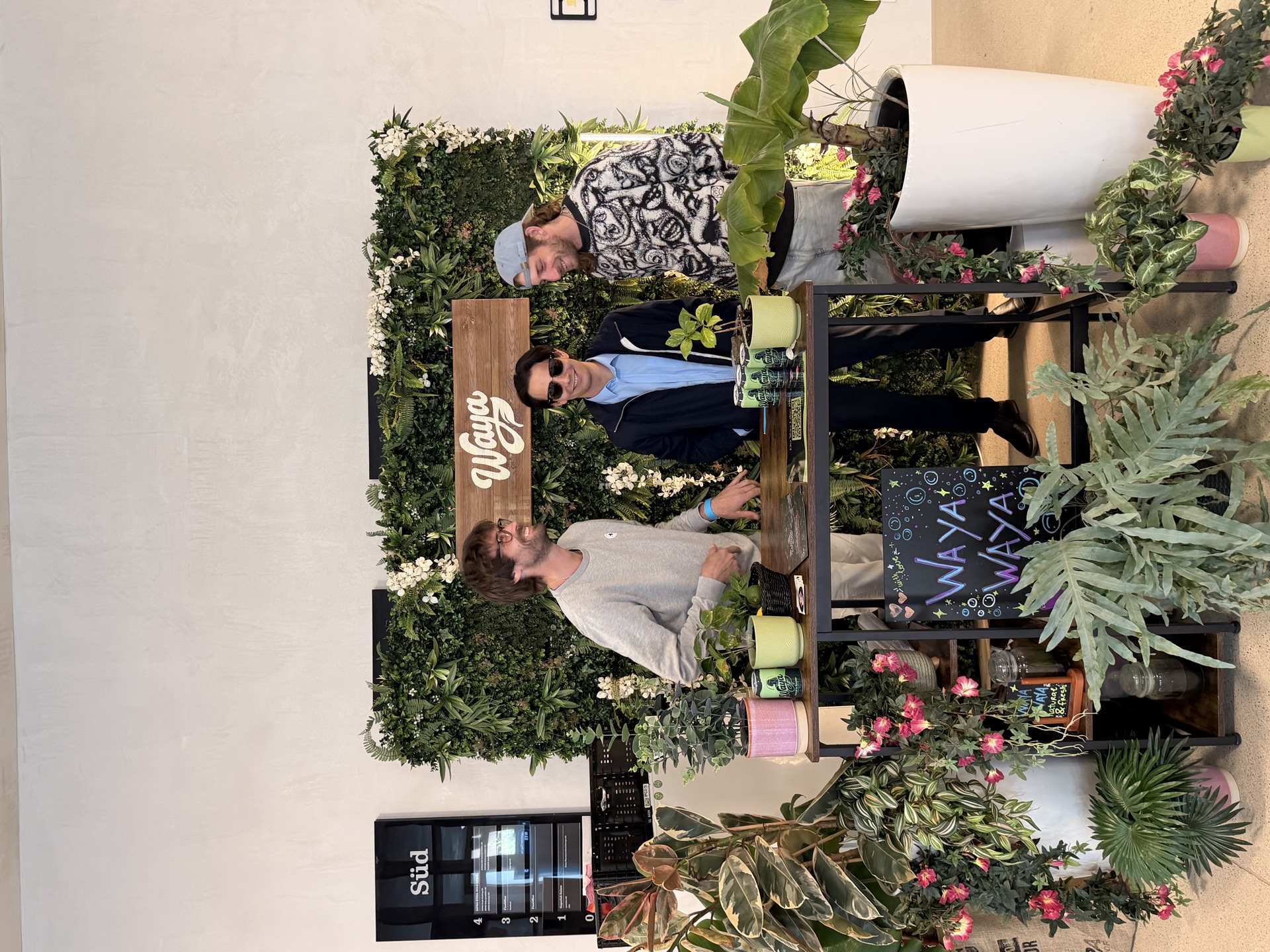 Das WAYA Team vor der grünen Blumenwand mit WAYA-Schild