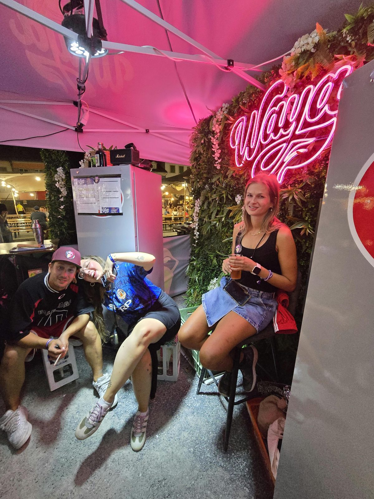 Lounge am WAYA-Stand mit pinkem Neon-Logo und Blumenwand