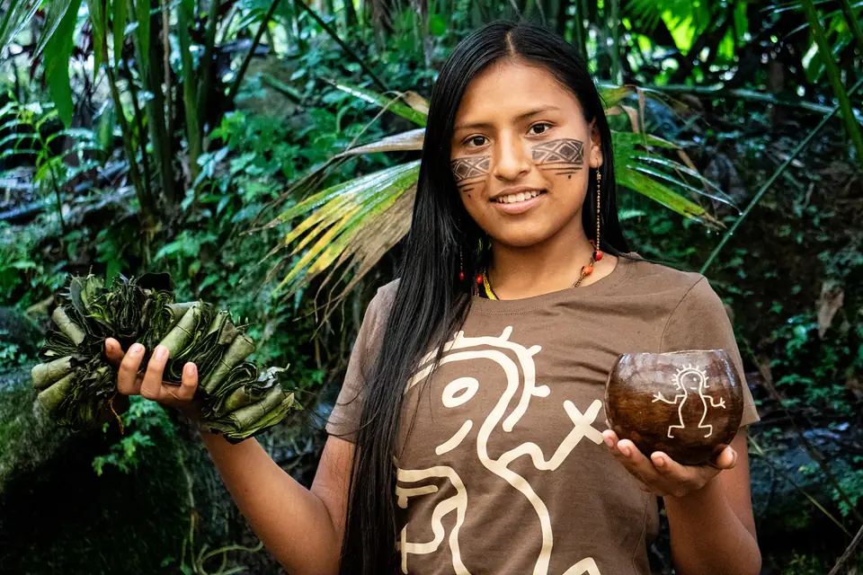 Junge Kichwa-Frau mit einem Bündel Guayusa-Blätter und einer Kalebasse